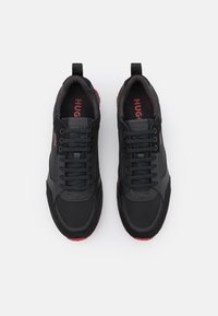 Baskets noires avec tissu texturé et dessus en cuir, dotées d'un bout rond, de lacets noirs, d'accents rouges et d'une semelle en caoutchouc.