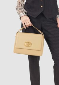 Borsa a tracolla in pelle beige con un design strutturato, dotata di un logo dorato prominente, manico corto e chiusura a pattina. Superficie testurizzata.