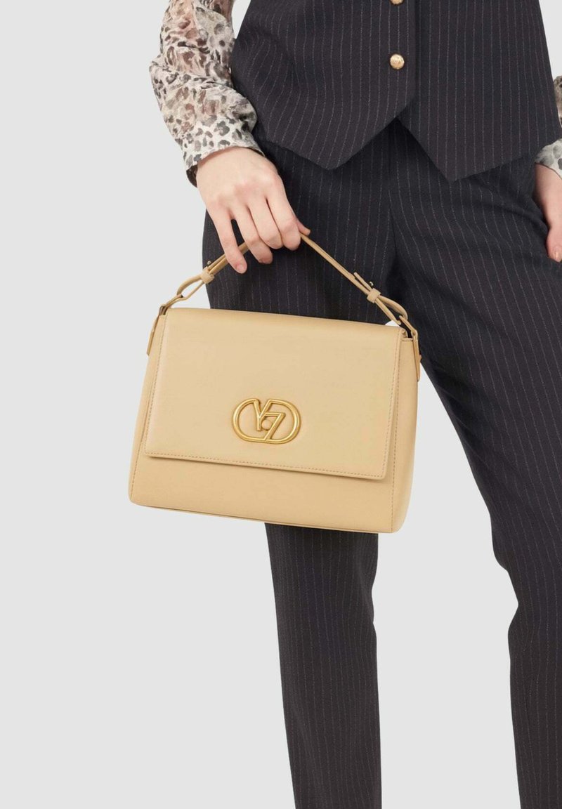 Borsa a tracolla in pelle beige con un design strutturato, dotata di un logo dorato prominente, manico corto e chiusura a pattina. Superficie testurizzata.