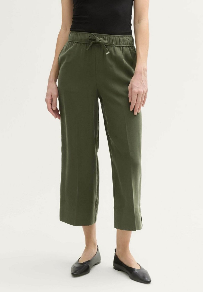 Grüne, kurze Hosen mit einem Zugbandbund, die locker sitzen und seitliche Schlitze am Saum aufweisen; kombiniert mit schwarzen, flachen Schuhen.