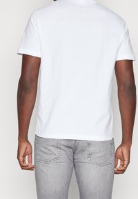 Camiseta blanca de algodón con mangas cortas, cuello redondo y corte recto, combinada con unos jeans de mezclilla gris claro con bolsillos traseros.