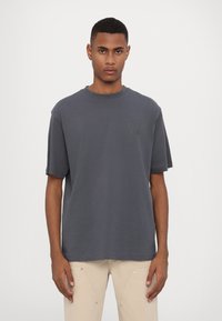 Dark grey T-shirt made of cotton, featuring a round neck and short sleeves. A subtle logo is printed on the left chest area.