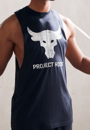 Muskularna osoba ubrana w czarny, bezrękawnik z białym, postarzanym logo byka oraz napisem „PROJECT ROCK” na przodzie.