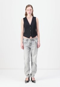 Schwarze Nadelstreifen-Weste mit V-Ausschnitt und Knöpfen vorne, kombiniert mit hellgrauen geraden Jeans und schwarzen patentierten Lederabsätzen.