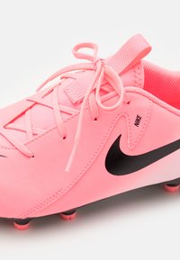 Crampons de football Nike roses avec une tige synthétique lisse, présentant un swoosh noir, des lacets plats et une semelle intérieure texturée. Dots en caoutchouc sur la semelle.