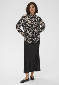 Juoda ilgomis rankovėmis palaidinė su balta abstrakčių lapų raštu, derinama su elegantiška juoda satino maxi suknele ir juodais balerinomis. Lygi tekstūra, laisvas kirpimas.