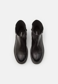 Bottes de cheville en cuir noir avec une texture lisse, bout rond, fermeture zip et poignets rembourrés. Présente une finition contrastante mate et brillante.