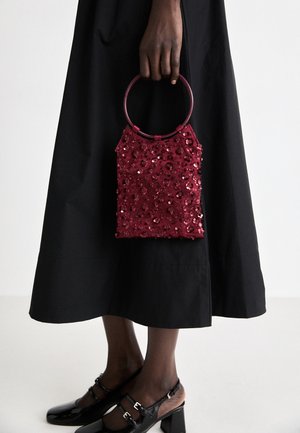 Borsa a tracolla bordeaux in paillettes con manico circolare, forma rettangolare e superficie testurizzata; abbinata a una gonna nera e scarpe nere lucide.