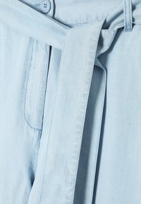 Lichtblauwe spijkerbroek met een gestrikt riem, voor zien van een voorzak, een gladde textuur en zichtbare stiksels langs de naden.