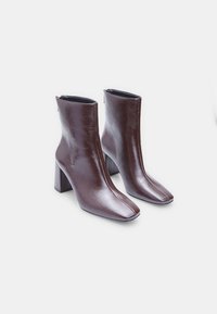 Brown leather ankle boots with a square toe, sleek design, and block heels, featuring a smooth texture and zip closure at the back.