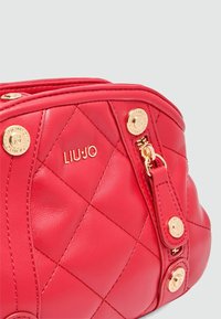 Rote gesteppte Lederhandtasche mit goldenen Beschlägen, Logodetail und einem Reißverschluss mit dekorativem Ziehband. Kompaktes Design und glatte Textur.