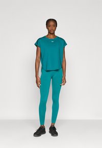 Τυρκουάζ αθλητικό τοπ με κοντά μανίκια, σετ με ταιριαστά τυρκουάζ κολάν. Και τα δύο έχουν απαλό ύφασμα, με απλό σχέδιο χωρίς μοτίβα.