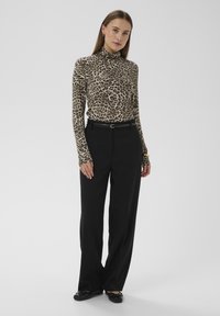 Rollkragenoberteil mit Leopardenmuster aus weichem Stoff, kombiniert mit hoch taillierten schwarzen Hosen und schwarzen flachen Schuhen, mit einem schmalen Gürtel versehen.