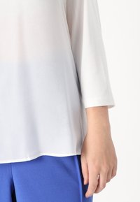 Witte, lichte blouse met driekwart mouwen, met een gebogen zoom en een gladde textuur. Gekozen met effen blauwe broek.