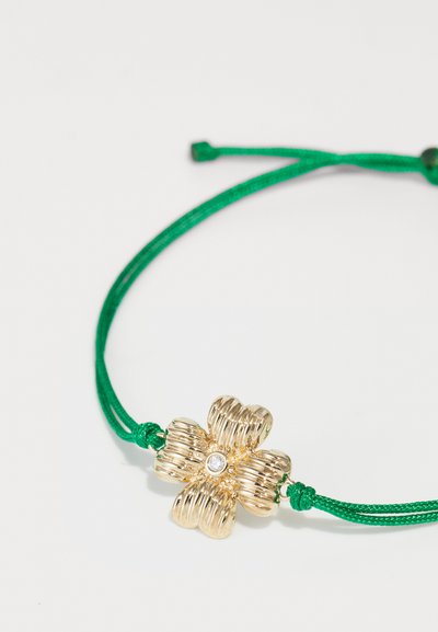 Gold flower-shaped bracelet with textured petals, featuring a central clear gemstone, attached to a green adjustable cord.