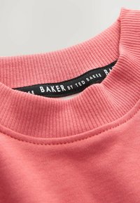 Roze sweatshirt met een geribbelde halslijn, voorzien van een zwart label met de tekst "BAKER by TED BAKER." De stof lijkt zacht met zichtbare stiksels.