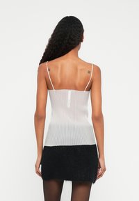 Hvitt ribbet tanktop med tynne stropper, med en subtil tekstur og glidelås bak, kombinert med et svart fluffy miniskjørt.