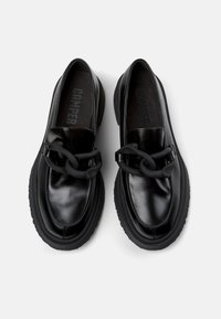 Schwarze Leder-Slipper mit einer klobigen schwarzen Sohle und einem auffälligen Kettendetail über der Vorderseite, mit einer glatten und glänzenden Oberfläche.