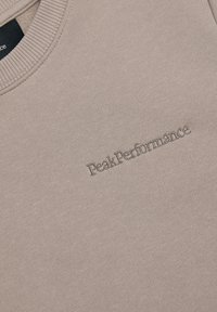 Pullover sweatshirt in gedempt beige stof, met een ribgebreide halslijn en een reliëf "Peak Performance" logo aan de voorkant.