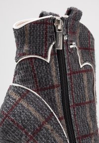 Gray and brown plaid textile with white accents, featuring a zipper closure and a distinct collar design. Material appears textured and thick.