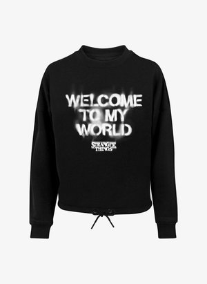 Melnā sportiskā džemperī ar baltu uzrakstu "LAIPNI LŪDZAM MANĀ PASAULĒ", aprīkots ar saistošu apakšmalu, apaļu kakla izgriezumu un garām piedurknēm. Izgatavots no mīksta materiāla.