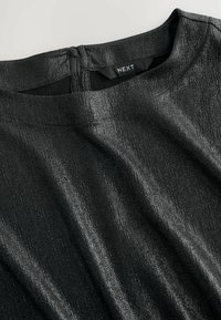 Blusa nera con texture e una leggera lucentezza, caratterizzata da scollatura rotonda e chiusura posteriore. Realizzata in tessuto leggero con una morbida caduta.