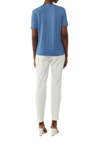 Niebieska koszula z krótkim rękawem z miękkiego materiału, w połączeniu z slim fit białymi spodniami i jasnymi sandałami na koturnie. Prosty design, bez wzorów czy akcentów.