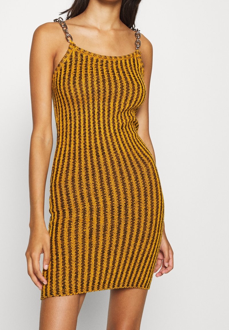 Gebreide jurk met een aansluitende vorm, voorzien van verticale gele en zwarte strepen, dunne bandjes en metallic accenten op de schouder.