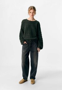 Donkergroen, gestructureerd sweatshirt met losse mouwen, gecombineerd met donkere denimbroek en tan instappers. Eenvoudig en ontspannen outfitontwerp.