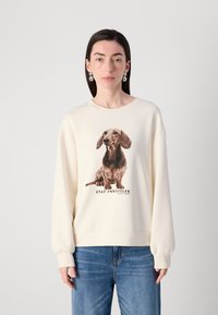 Beige sweatshirt lavet af blødt stof med et trykt dachshund-design og teksten "STAY PAWSITIVE", med ribbede mansjetter og kant.
