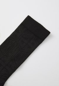Sosete negre dintr-un material texturat, având un model geometric și o manșetă ribbed mai groasă în partea de sus.