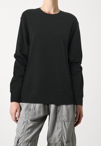 Svart sweatshirt med långa ärmar och rundad nacke, tillverkad av mjukt tyg. Har en avslappnad passform och ribbade mudd-armar, bärs tillsammans med grå cargobyxor.