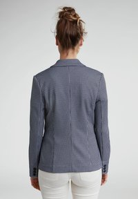 Veste blazer en pied-de-poule bleu marine et blanc avec revers structurés, coupe ajustée et poignets boutonnés, vue de dos.