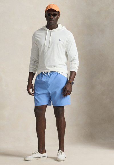 Light beige hoodie with drawstrings, blue swim shorts with logo, white sneakers, orange cap, and sunglasses. Simple design, casual attire.