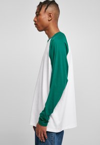 Weißes und grünes Langarm-T-Shirt mit Rundhalsausschnitt, mit kontrastierenden Ärmeln und lockerer Passform, aus weichem Baumwollmaterial gefertigt.