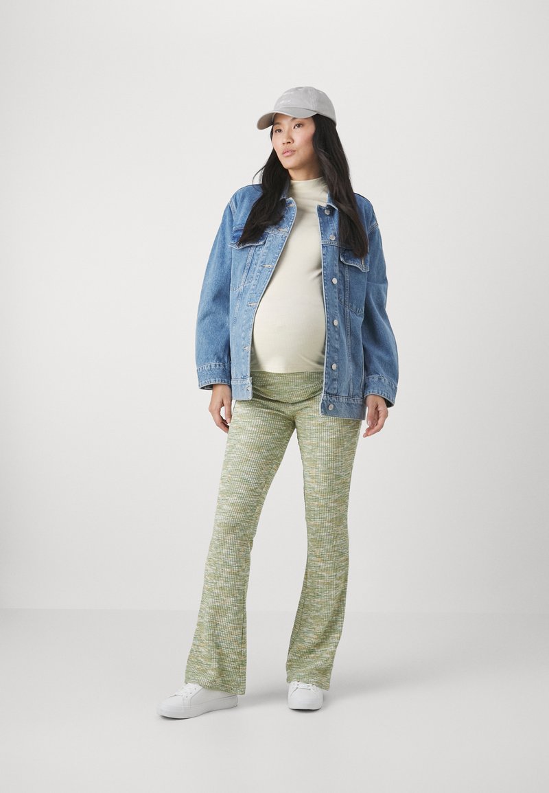 Denim jacket, cream top, patterned green flared pants, white sneakers, and a grey cap. The outfit features a relaxed fit and varying textures.