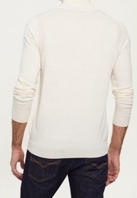 Light cream pullover sweater with a ribbed texture and fitted cuffs, featuring a high neck and subtle shoulder detailing.