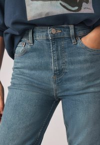 Šviesiai mėlyni džinsai su aukštu liemeniu, pagaminti iš džinso audinio; matomos siūlės ir priekinis sagų užsegimas; turi šonines kišenes.