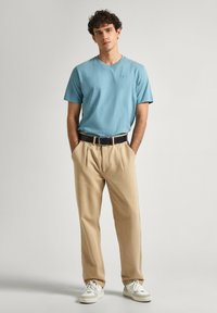 Jasnoniebieska koszulka z krótkim rękawem, beżowe spodnie w kant, czarny pasek i białe trampki. Gładka tekstura i luźny krój.