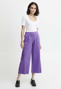 Pantaloni a gamba larga viola con vita alta, abbinati a un top aderente bianco a maniche corte e mocassini neri. Texture liscia, senza motivi.