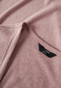 Maglione lavorato a maglia rosa chiaro con scollatura a V. Il tessuto ha una consistenza morbida e presenta un'etichetta che mostra i dettagli del marchio e della taglia.