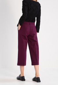 Bordeaux geknipte broeken met een relaxed fit, voorzien van zijzakken en een zachte textuur, gecombineerd met zwarte schoenen en een zwarte textuur top.