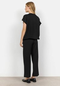 Top negro de corte suelto con mangas tipo cap sleeve y escote redondo, acompañado de pantalones negros rectos a juego y unos zapatos negros sencillos.