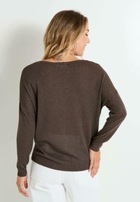 Suéter marrón de punto brillante con un escote ancho y mangas largas, ajustado en los puños. Diseño sencillo, adecuado para usar en capas.