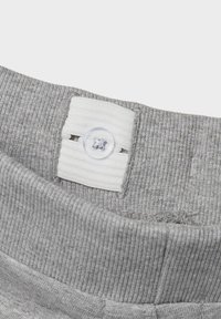 Ceinture élastique grise avec texture côtelée, comportant un onglet blanc et un bouton transparent. Gros plan sur le tissu et les détails de fermeture.