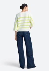 Pulover crem pufos cu dungi galbene îndrăznețe, mâneci largi și decolteu rotunjit, asortat cu blugi albastru închis, cu talie înaltă.
