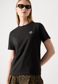 T-shirt in cotone nero con collo a giro, maniche corte e un piccolo logo geometrico bianco sulla parte superiore sinistra del petto.