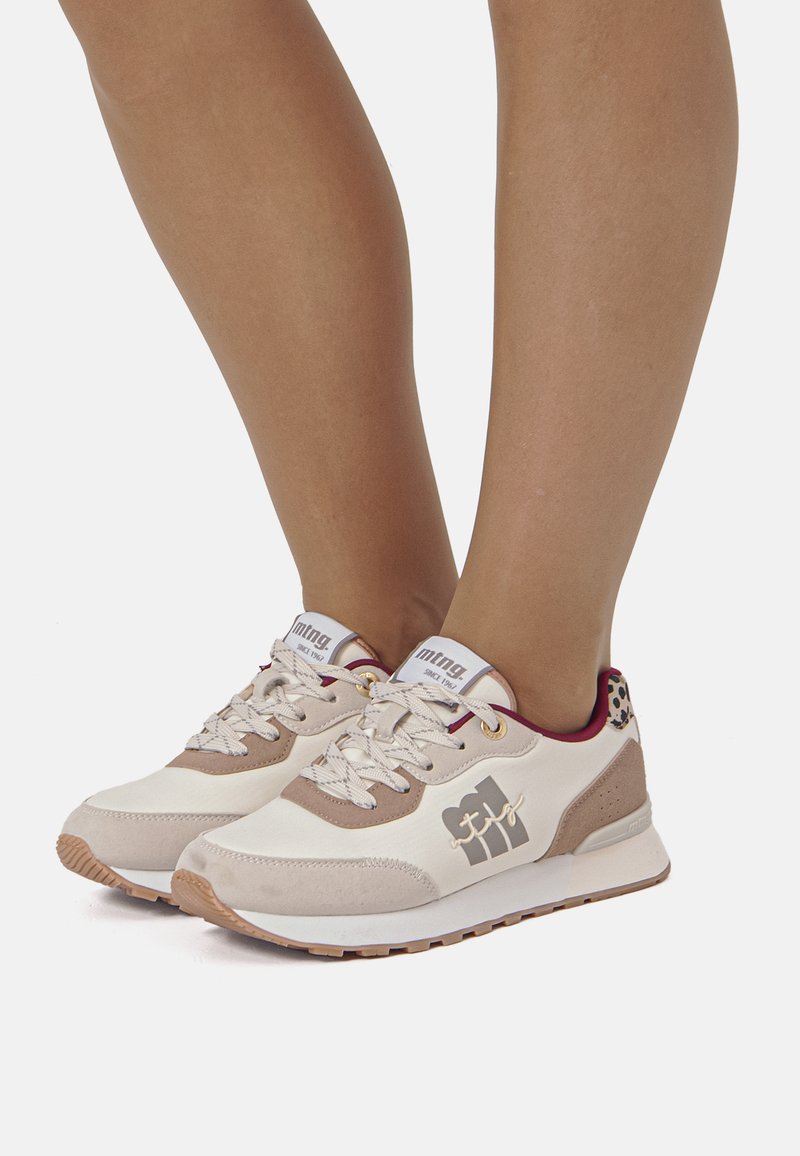 Sneaker mit cremefarbenem Obermaterial, braunen Wildlederakzenten, weißer Sohle und strukturiertem Schnürsenkel. Mit einem Logo an der Seite und einem gepolsterten Kragen.