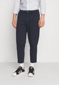 Marinblå, trånga byxor gjorda av lättviktig tyg; har en knappstängning och sidofickor; kombineras med svart och vit sneakers.