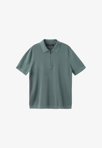 Camiseta tipo polo de manga corta color verde apagado con cuello y una cremallera corta en la parte delantera sobre un fondo blanco.